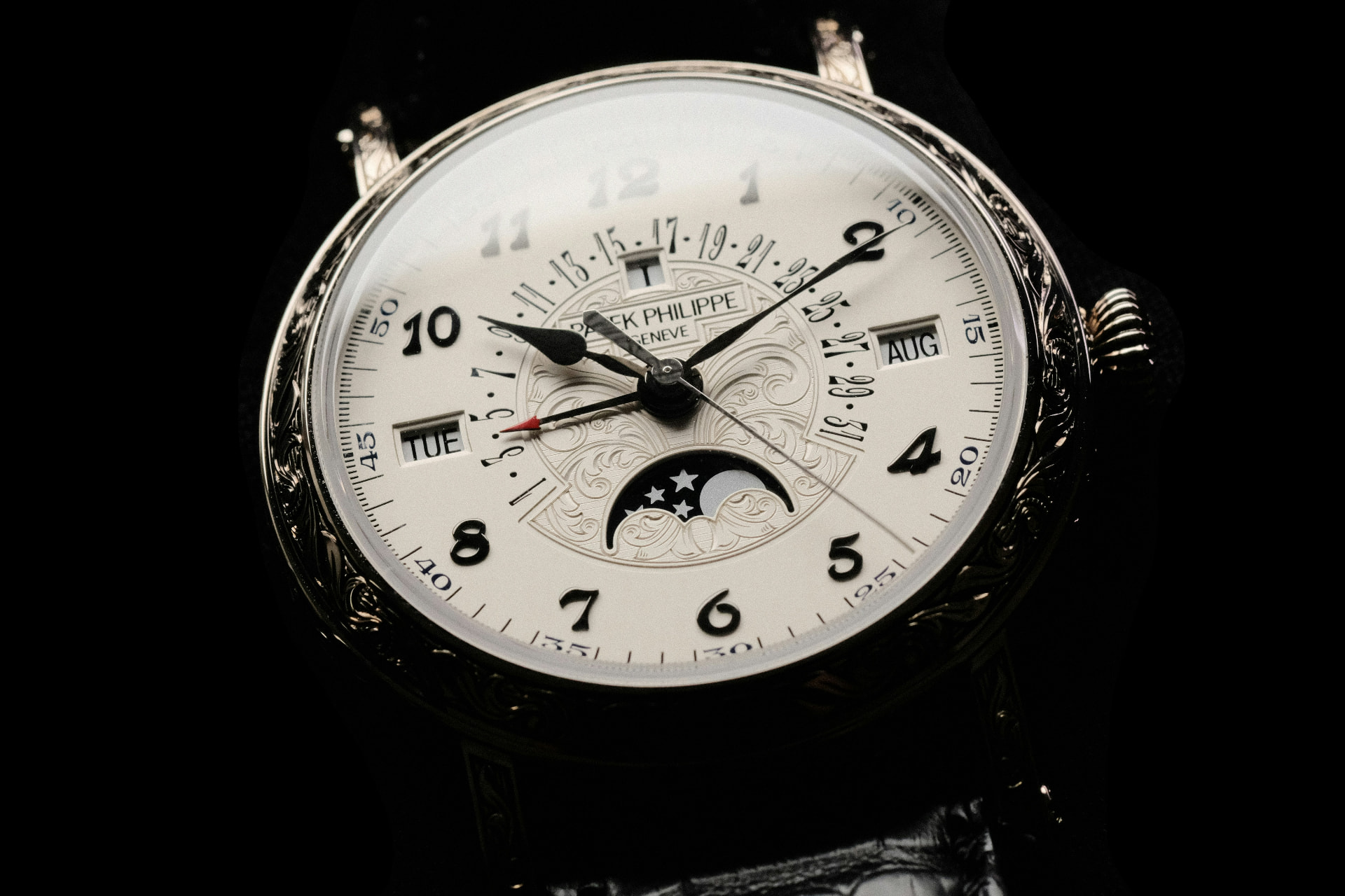 A close-up of an ornate Patek Philippe watch face against a dark background