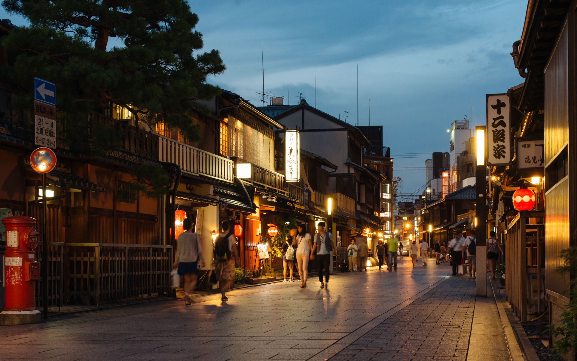 A quiet evening street in Kyoto, with warm lantern light and traditional wooden storefronts