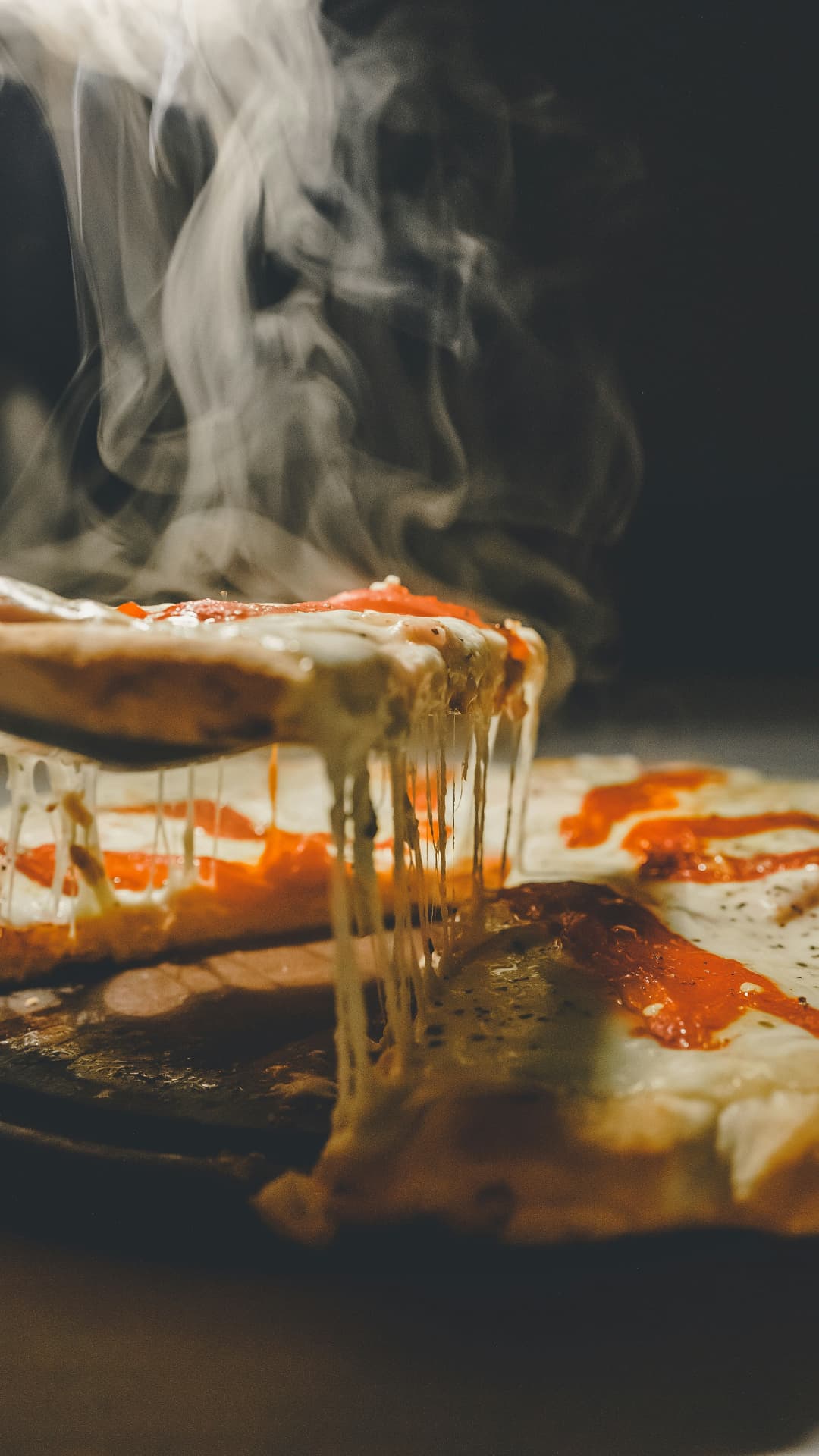 Steaming pizza slice lifted from a margherita pie with cheese pull