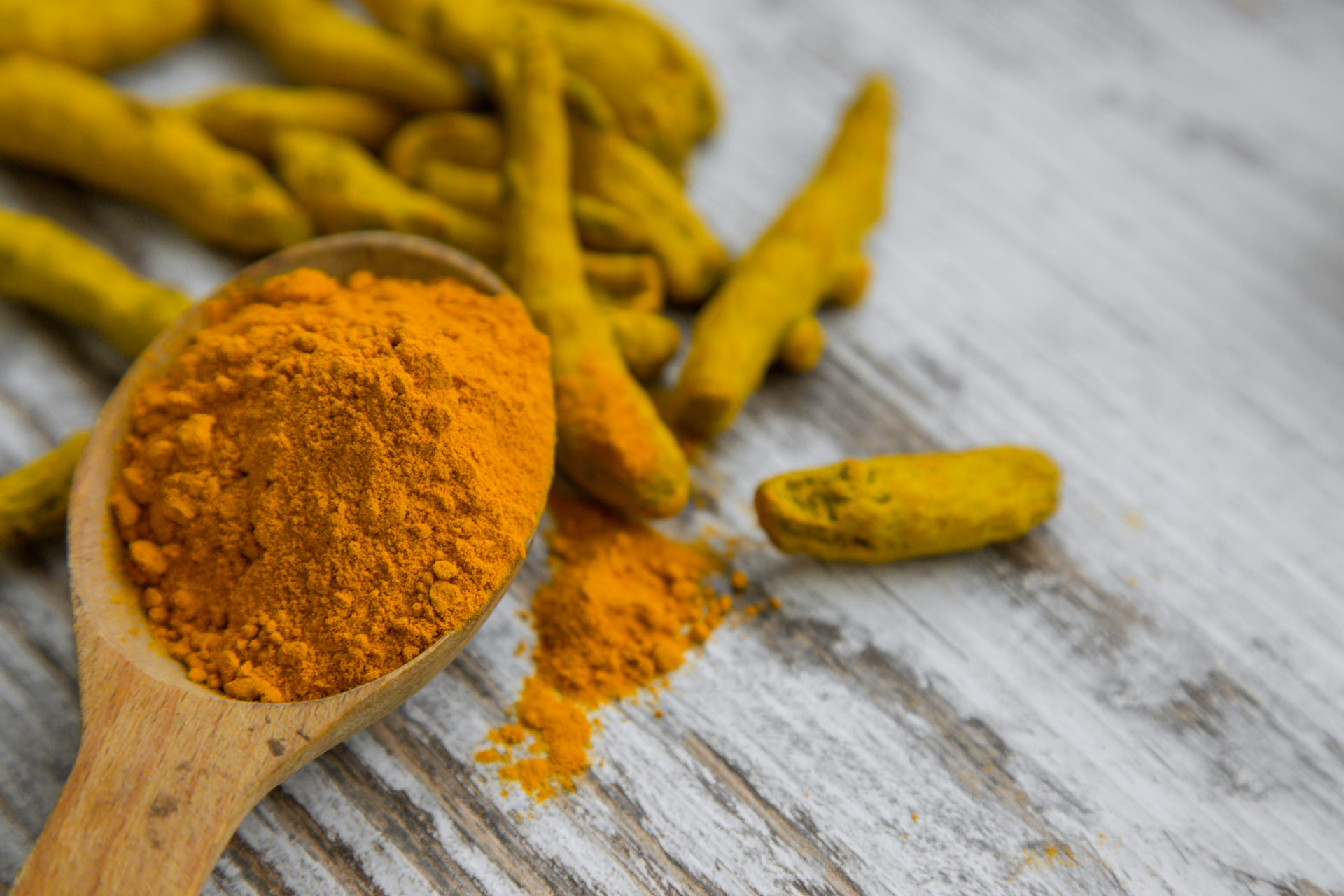 Ground turmeric on a wooden spoon beside fresh turmeric roots